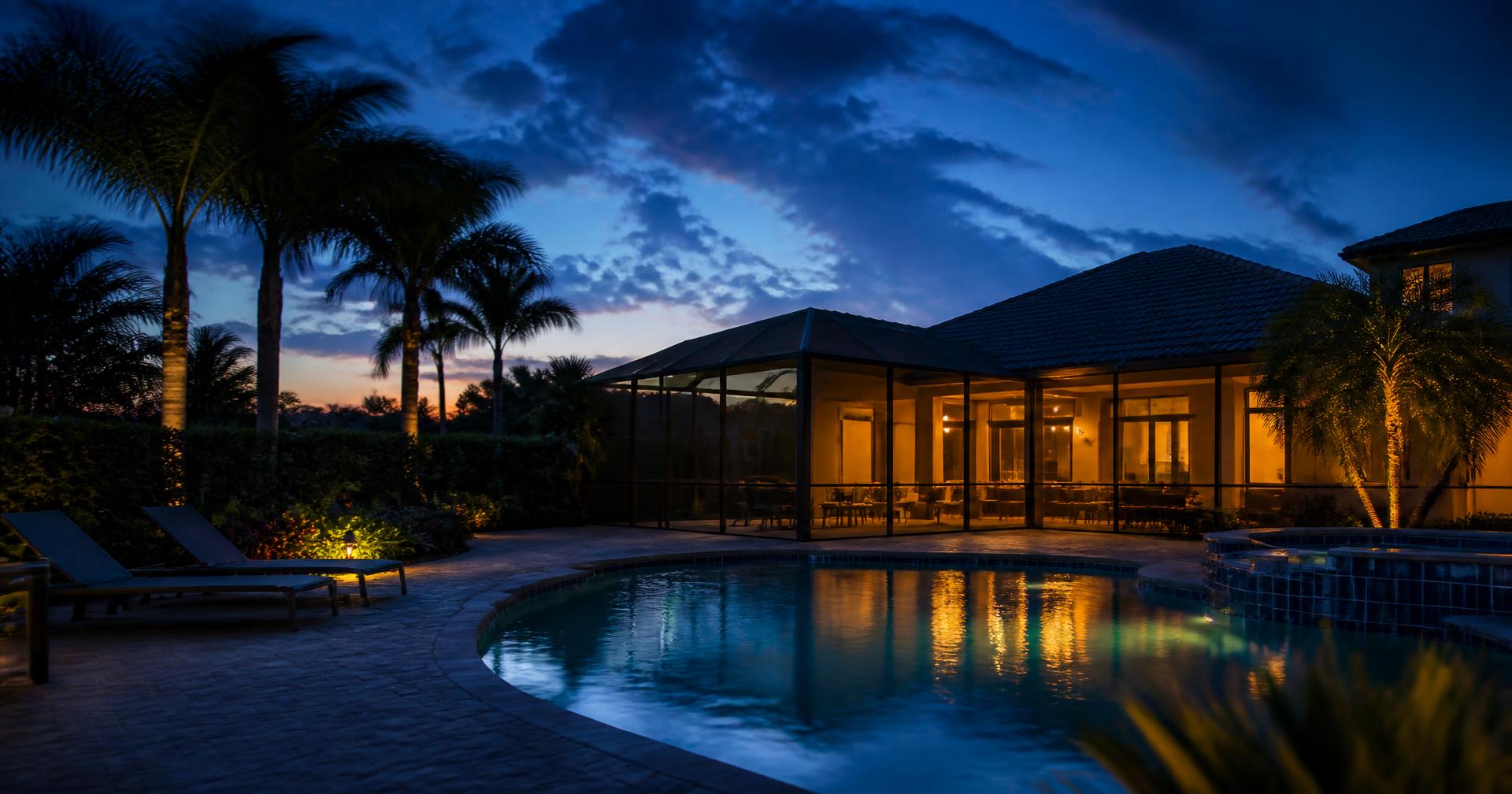 Florida backyard with an illuminated screened lanai and pool at dusk